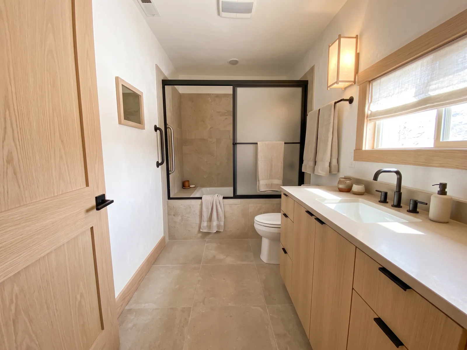 AI generated Japandi restyle of the same bathroom: white walls, pale oak door and vanity with a white top, pale stone floor and a paper wall light. Bath, shower doors, toilet and window stay in place.