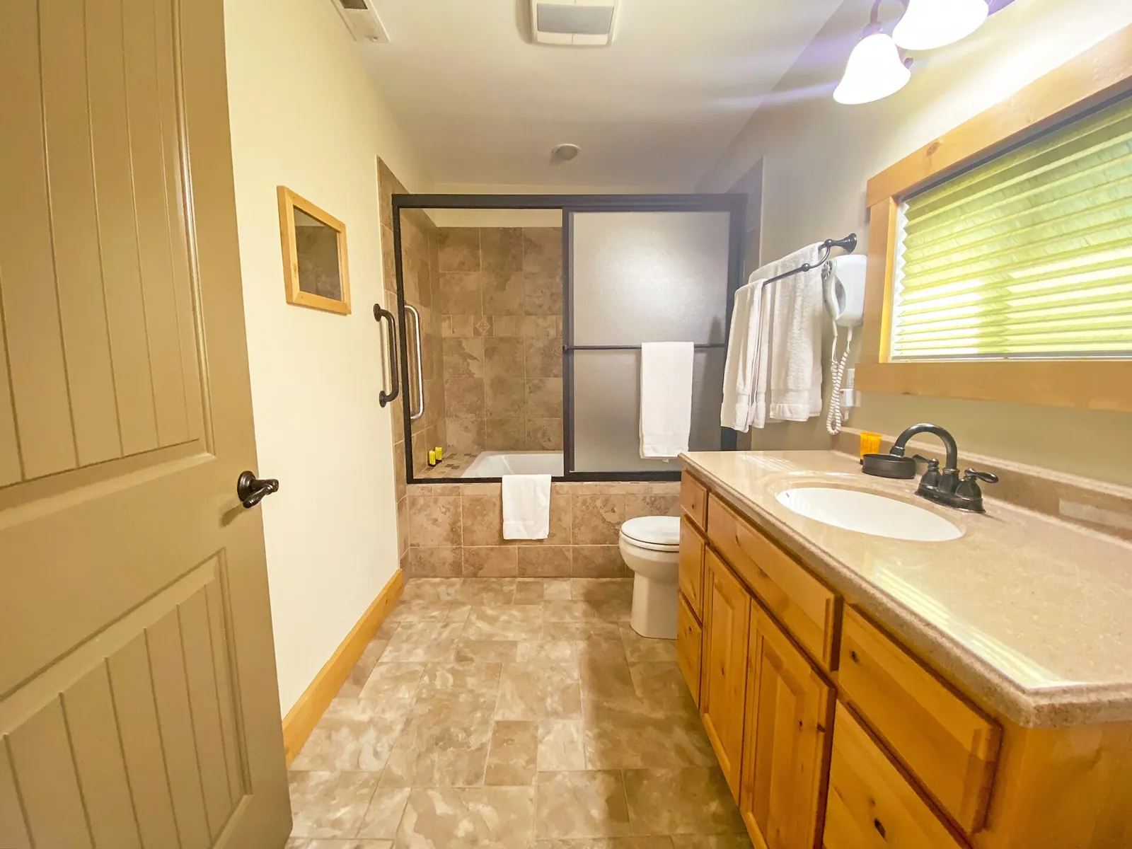Before: long bathroom with a pine vanity, a tiled bath with sliding shower doors and a window above the basin.
