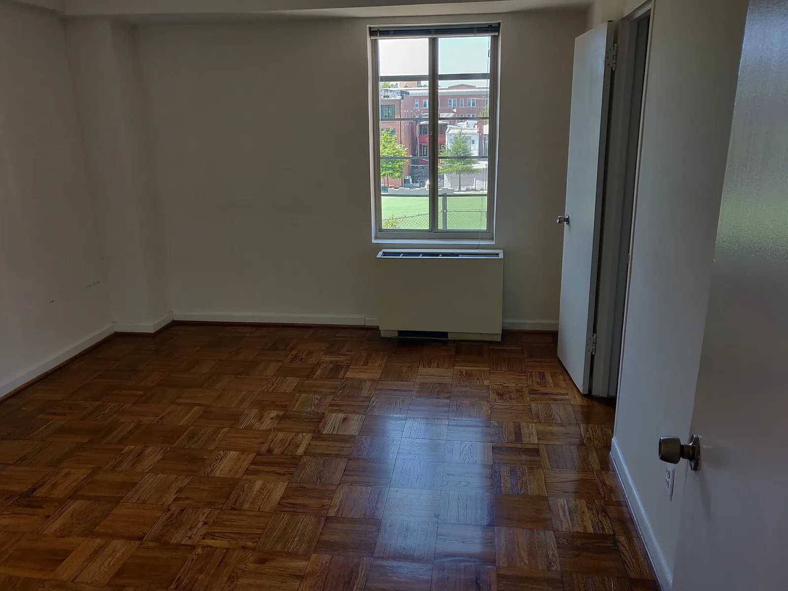 Before: empty bedroom with a parquet floor, one window above a radiator and two doors.